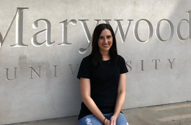 A smiling woman in front of a Marywood University sign.